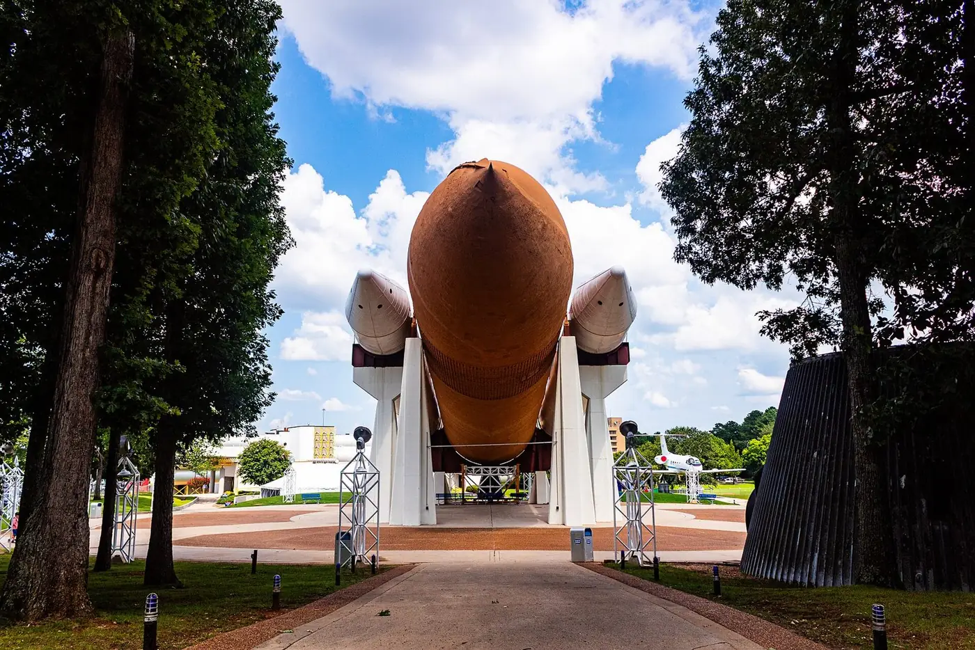Space shuttle stack display with an orange external tank, framed by tall trees
